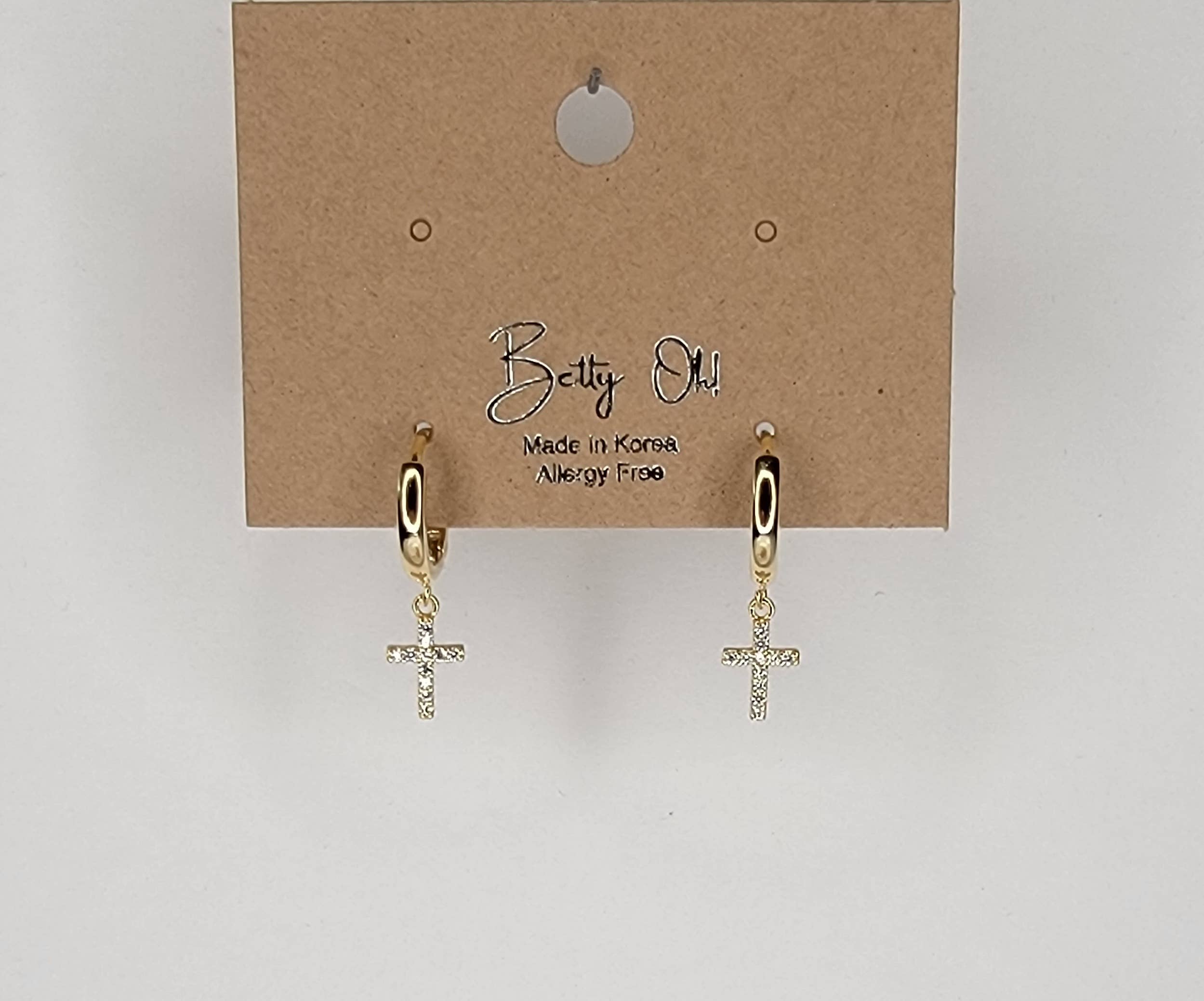 Gold cross earrings on a Betty Oh branded card against a light gray background