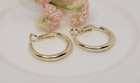 Gold hoop earrings on a white surface with pink flowers in the background
