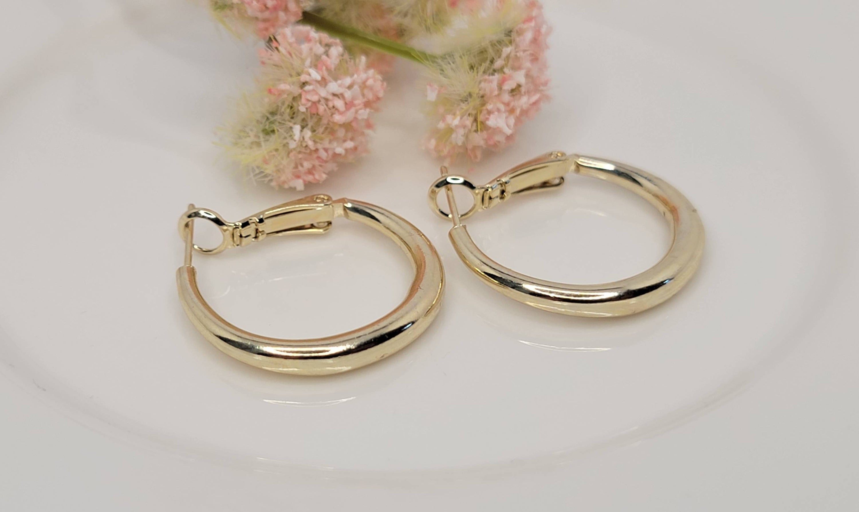 Gold hoop earrings on a white surface with pink flowers in the background