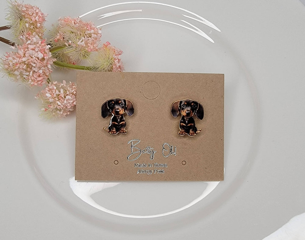 Dachshund-shaped earrings on a branded card with flowers in the background