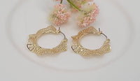 Gold hoop earrings on a white background with pink flowers.