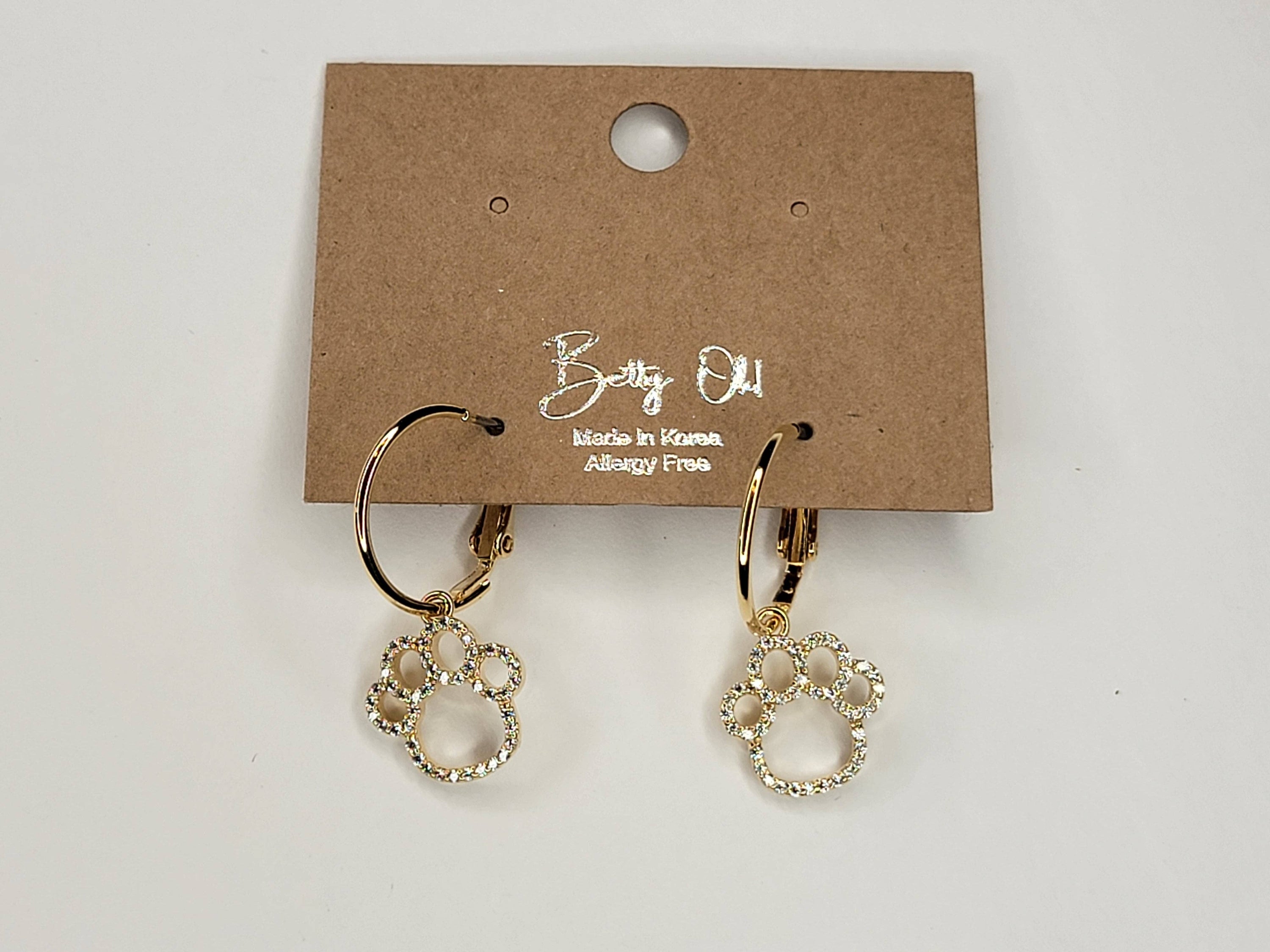 Gold hoop earrings with paw print charms on a Betty Oh branded card.