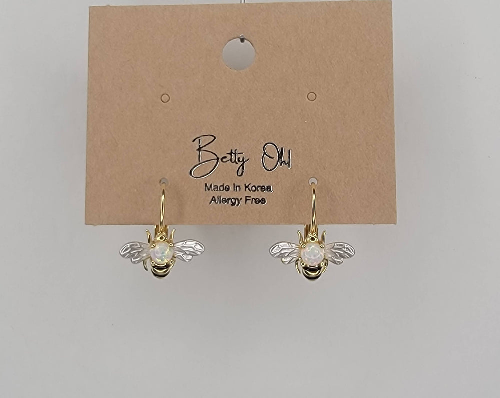 Gold bee-shaped earrings on a Betty Oh branded card against a gray background