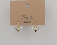 Gold bee-shaped earrings on a Betty Oh branded card against a gray background