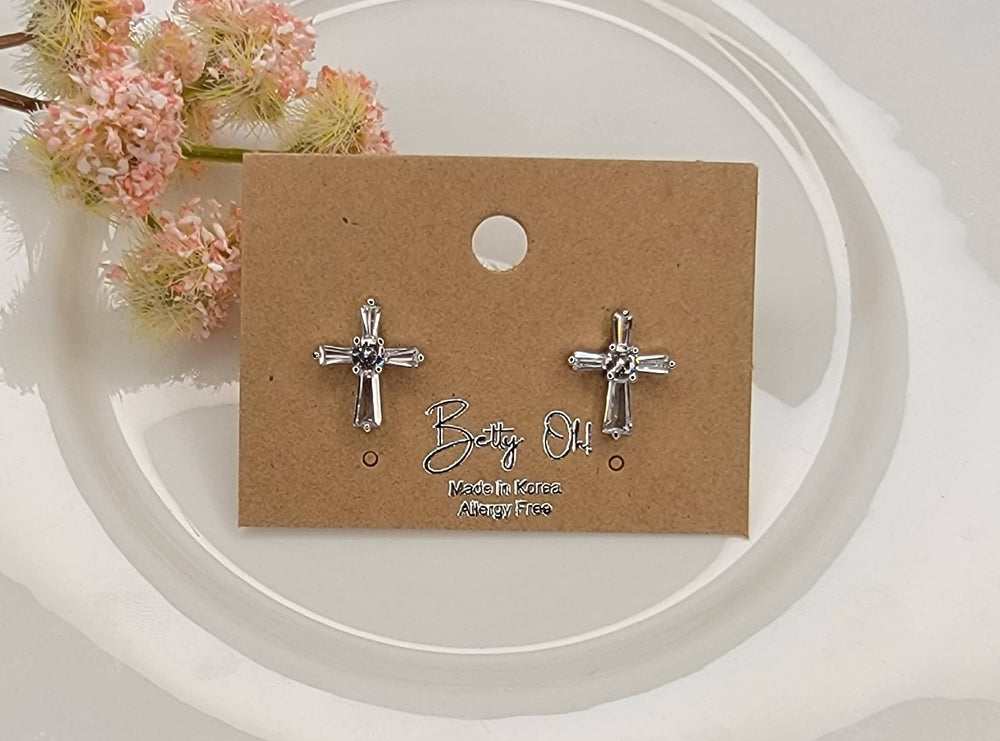 Silver cross earrings on a brown card with floral background