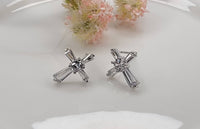 Silver cross-shaped earrings on a white surface with pink flowers in the background