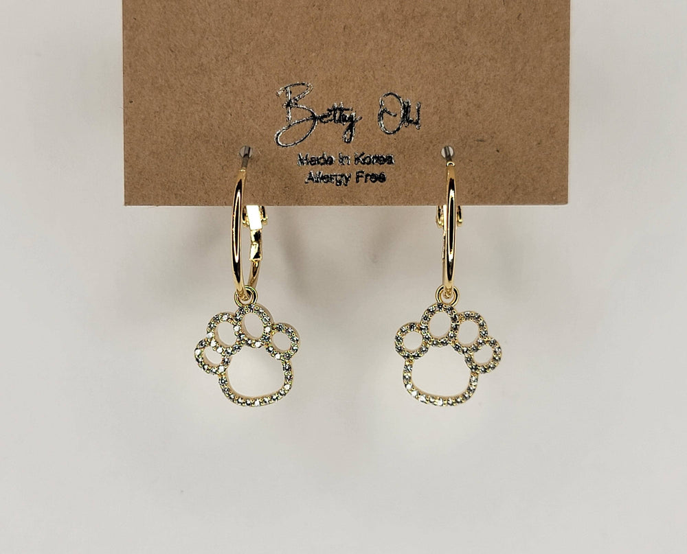 Gold paw print earrings on a brown card with 'Bella Bella' branding.