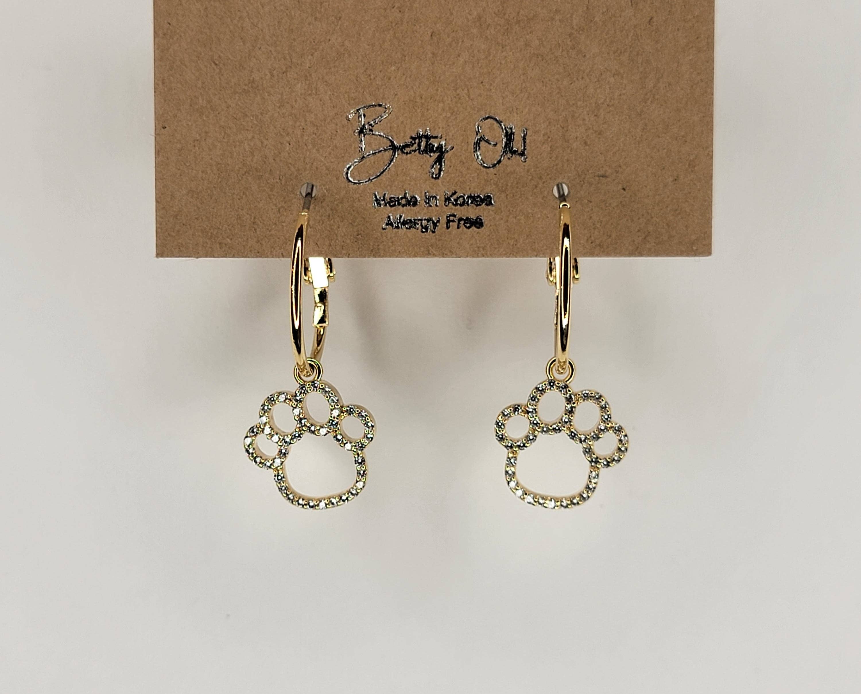 Gold paw print earrings on a brown card with 'Bella Bella' branding.