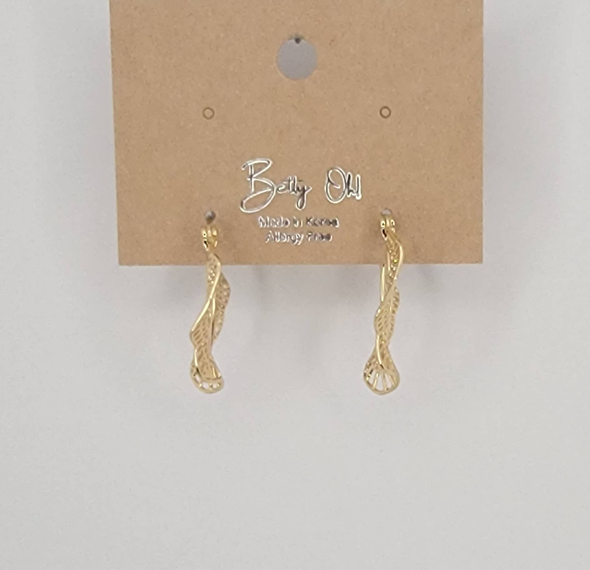 Gold earrings on a brown card with 'Betty Old' branding against a light gray background