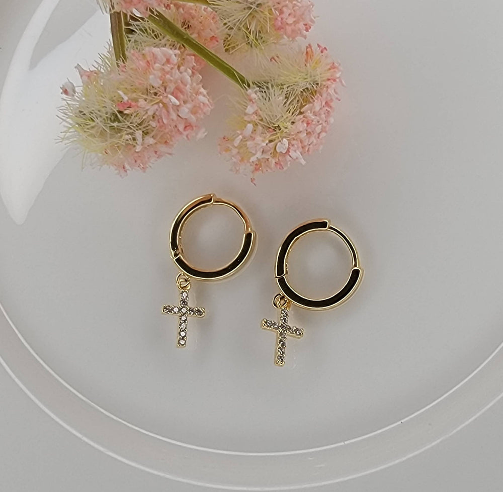 Gold hoop earrings with cross charms on a white surface with pink flowers.