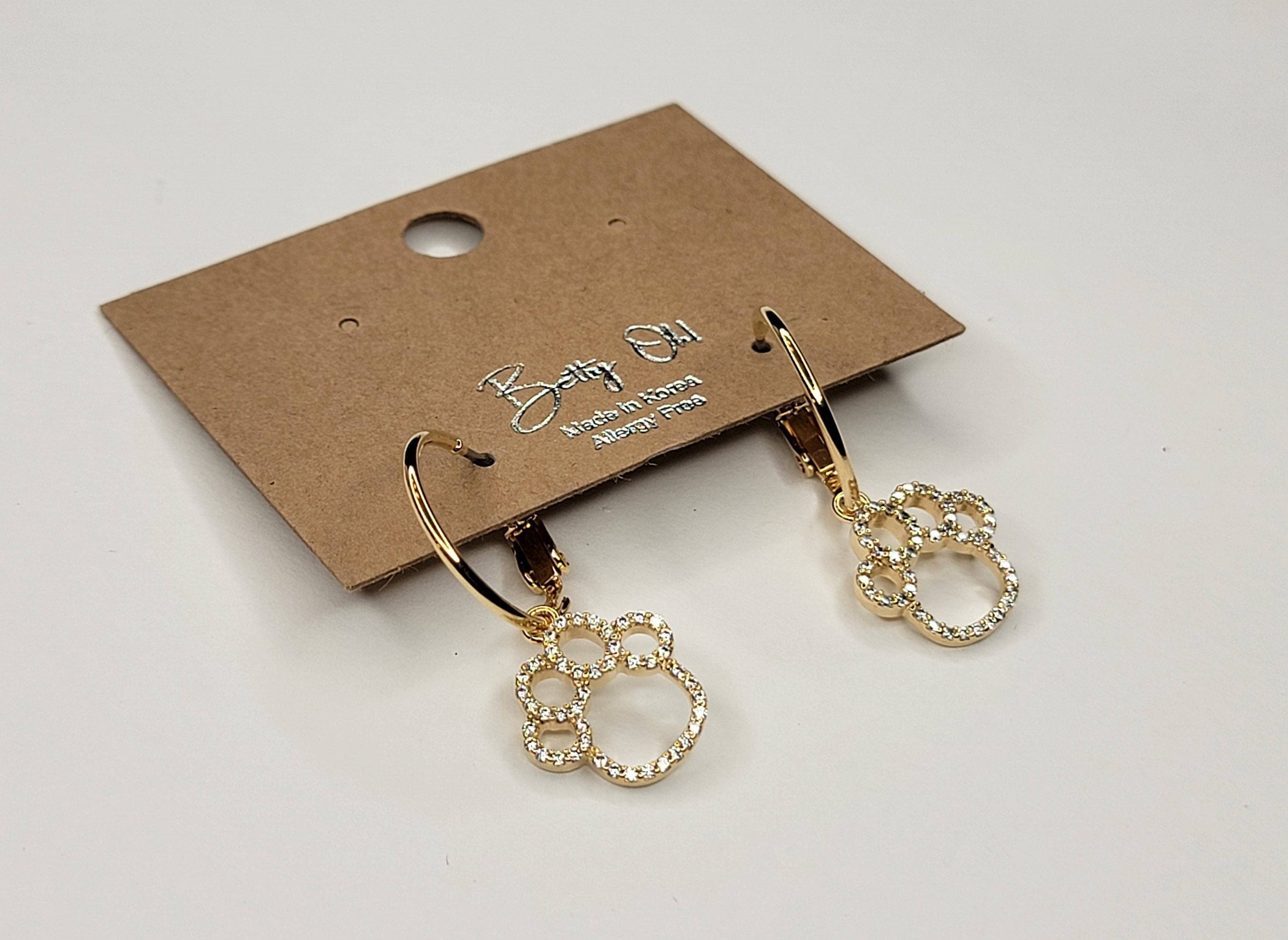 Gold earrings on a branded card against a light gray background
