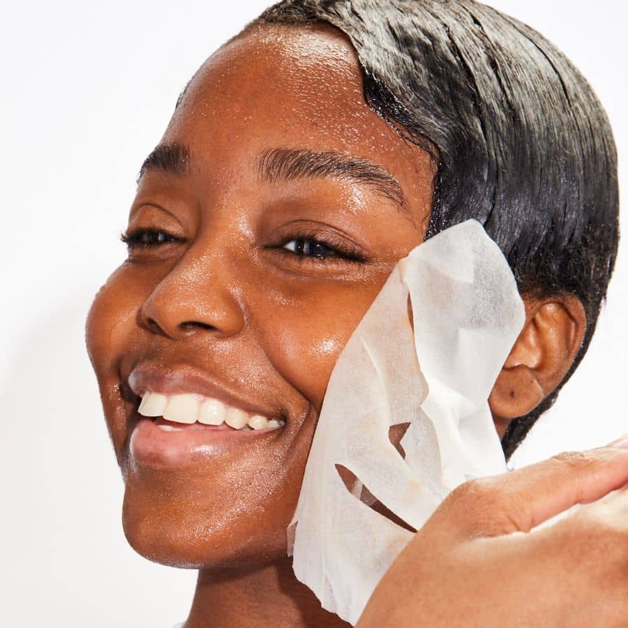 Woman applying a sheet mask to her face with a white background