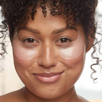 Woman wearing clear eye patches on a neutral background
