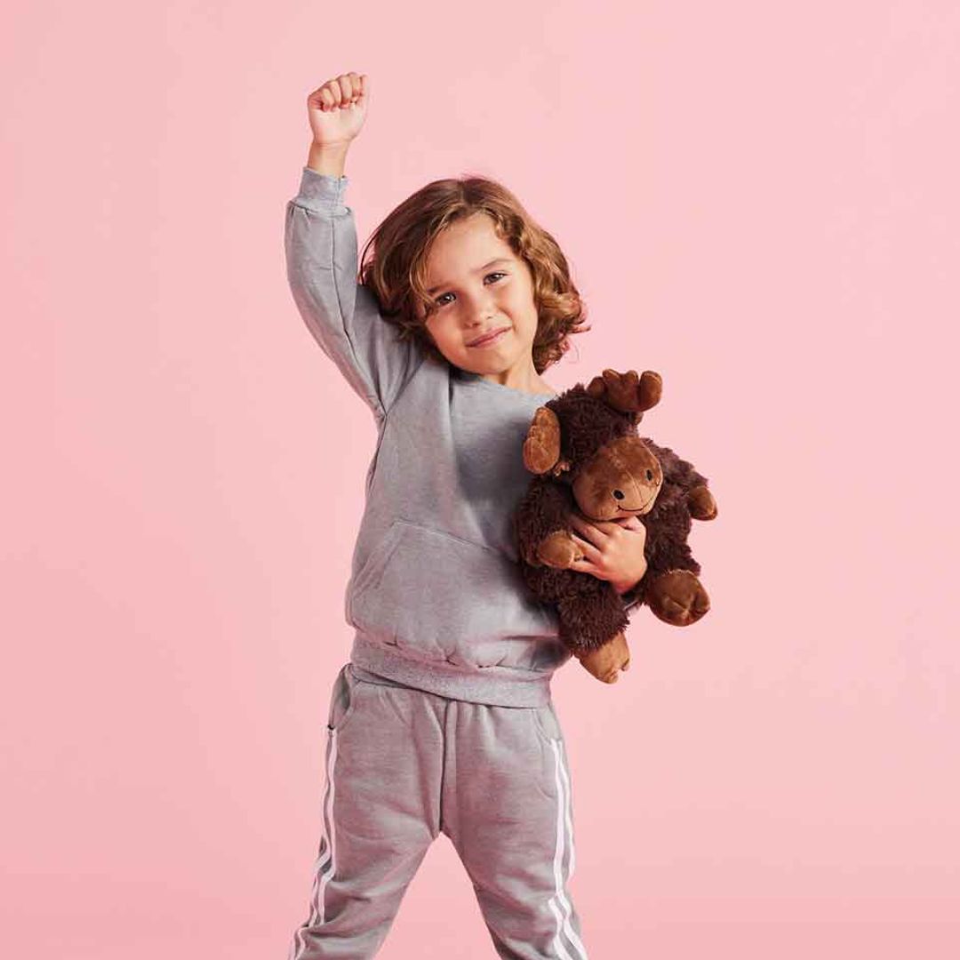 Child in gray tracksuit holding a moose against a pink background